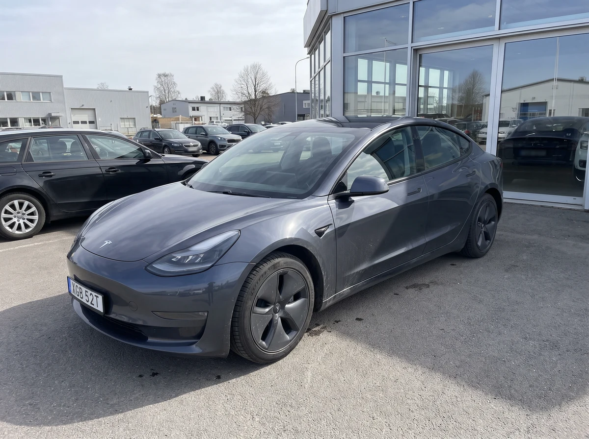 En grå Tesla Model 3 fotad med mobil utanför en bilhandlare